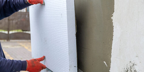 Construction,Worker,Installing,Styrofoam,Insulation,Sheets,On,House,Facade,Wall Verarbeitung einer Dämmplatte